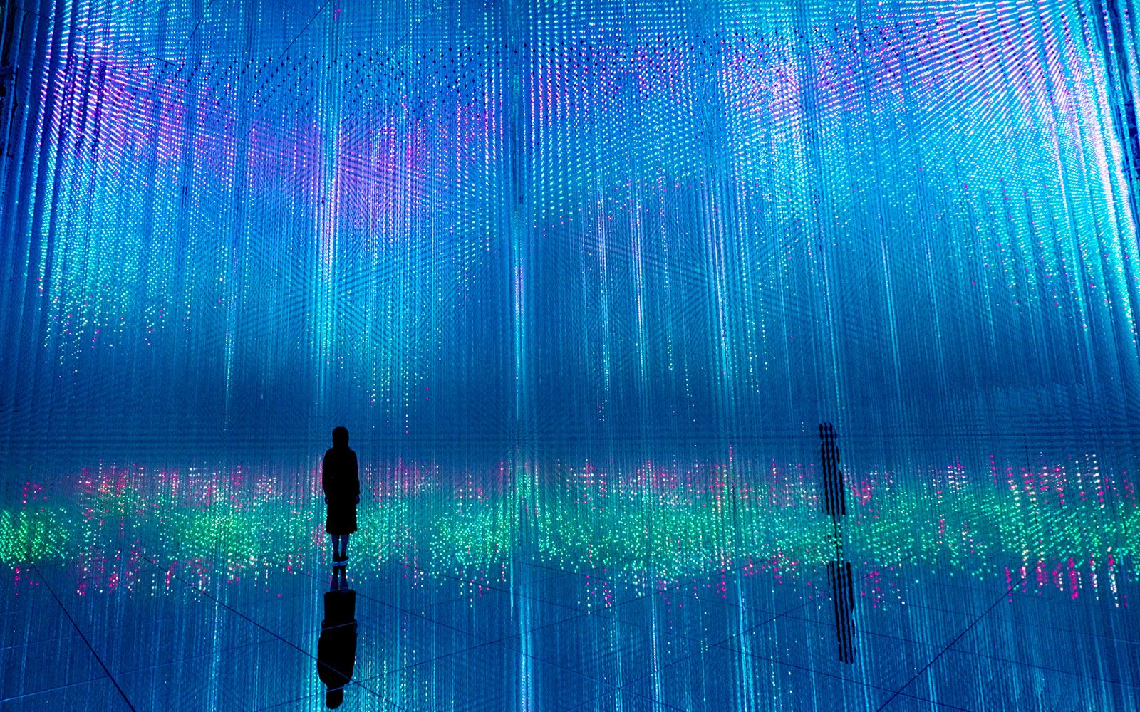 Blue, purple and green light pouring down and reflecting off a mirrored floor