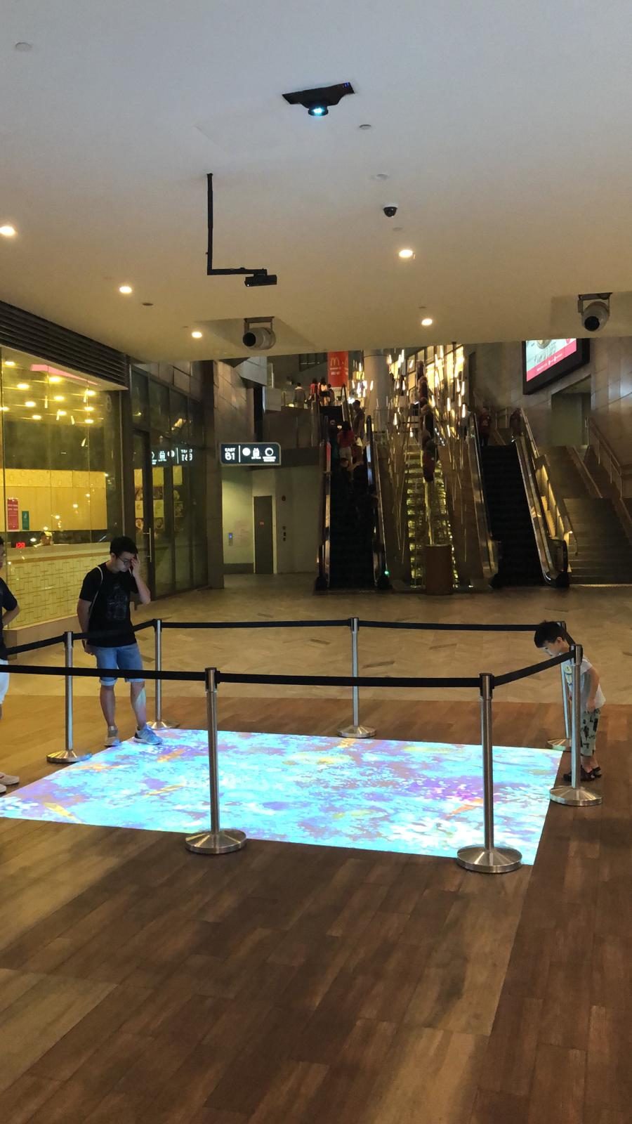 Interactive floor installation in a mall atrium with mounted projectors and barriers