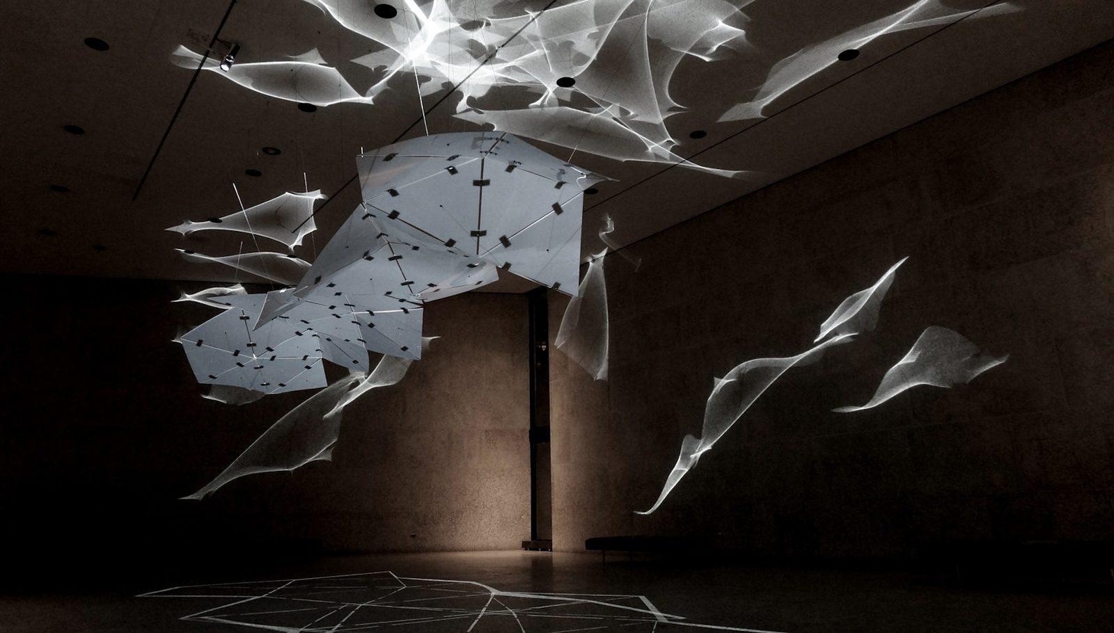 Abstract light patterns mapped along the structure of a dark exhibition wall