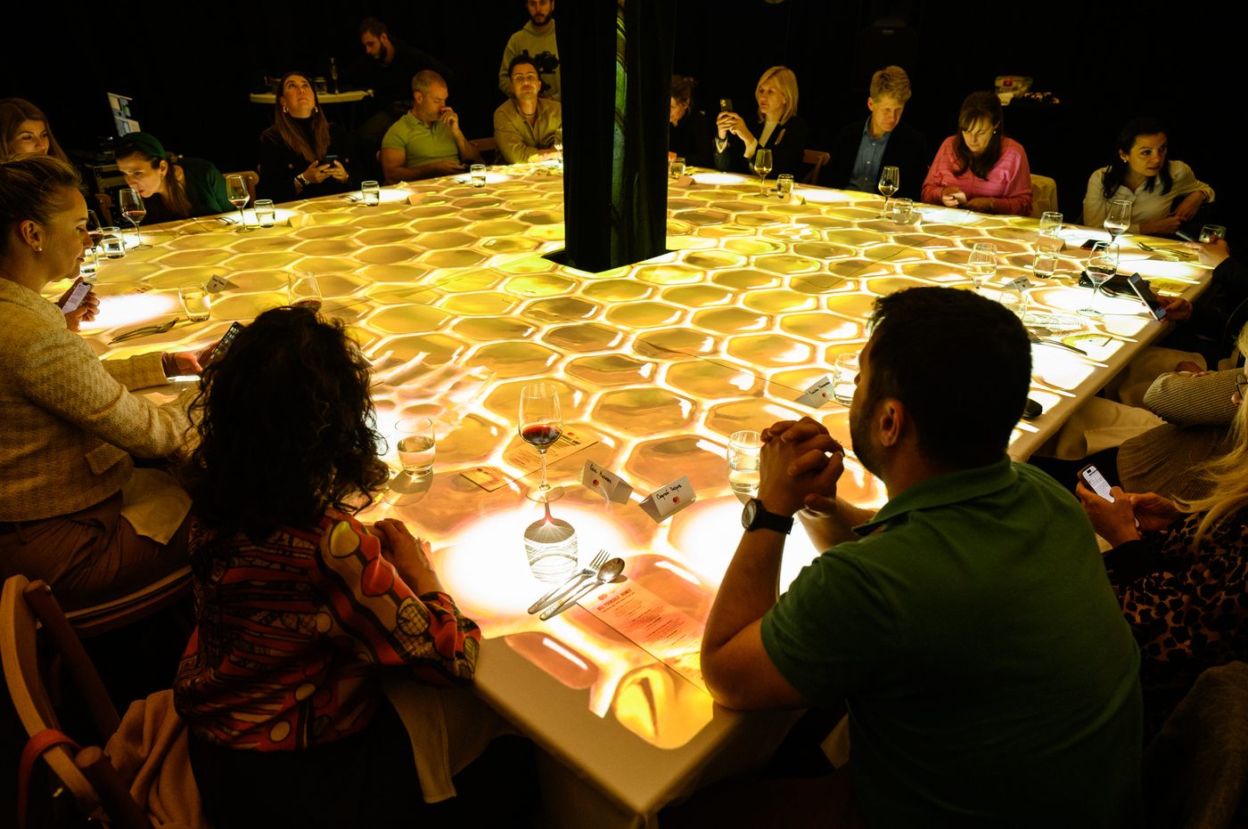 Guests dining around a projected table with a glowing honeycomb effect
