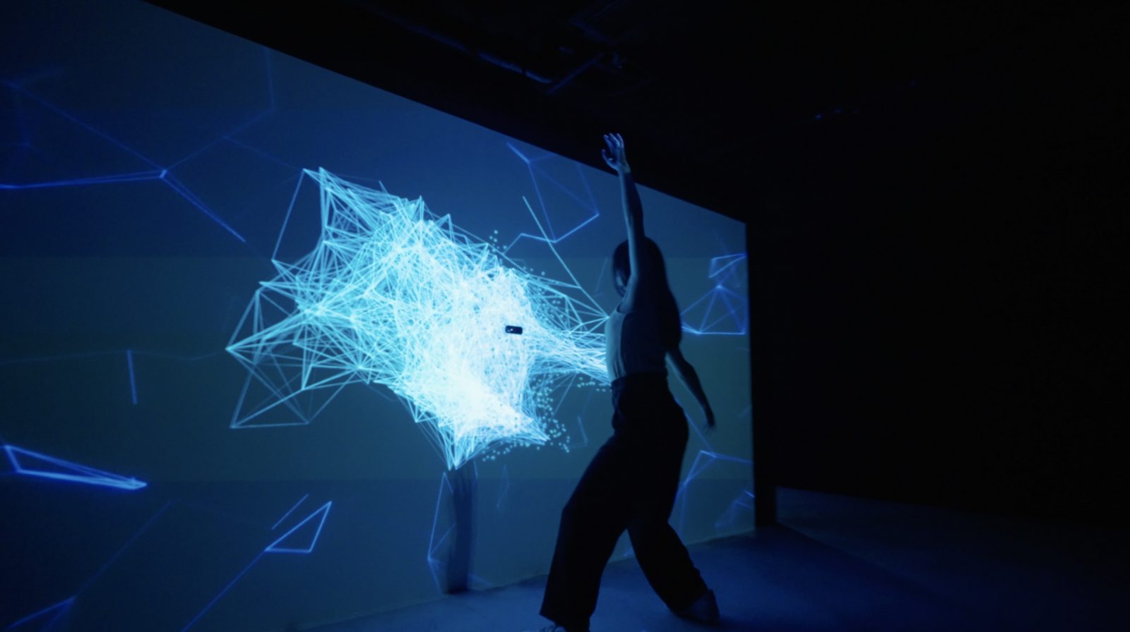 Dancer interacting with blue particle projection on a motion-sensing wall