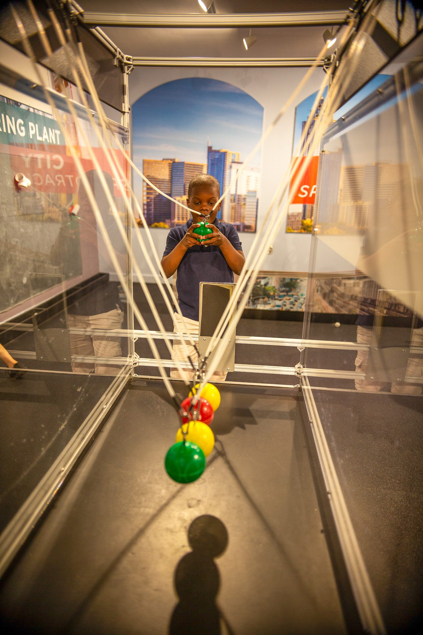 Boy operating a Newton's cradle hands-on exhibit at a science museum