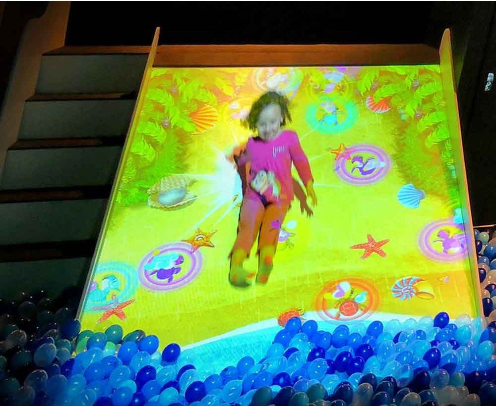 Child sliding from an interactive projection slide into a ball pool